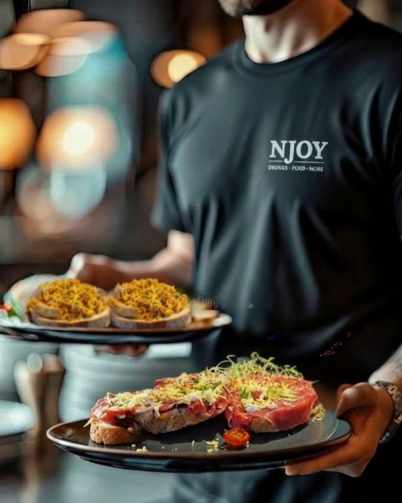 Medewerker van restaurant NJOY Kampen serveert lunchgerechten op borden, met zichtbaar NJOY-logo